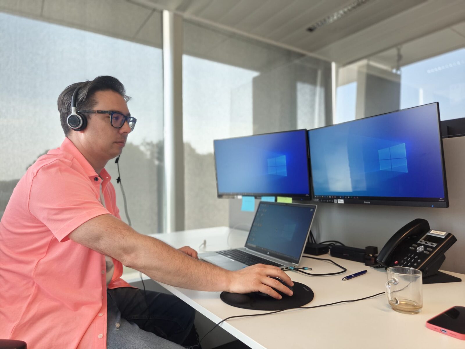 De helpdeskmedewerker van TSG, Darryl, aan zijn bureau. Hij werkt aan zijn computer en belt met klant om hem verder te helpen.